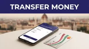 A smartphone with a money transfer screen beside a Hungarian bank card.