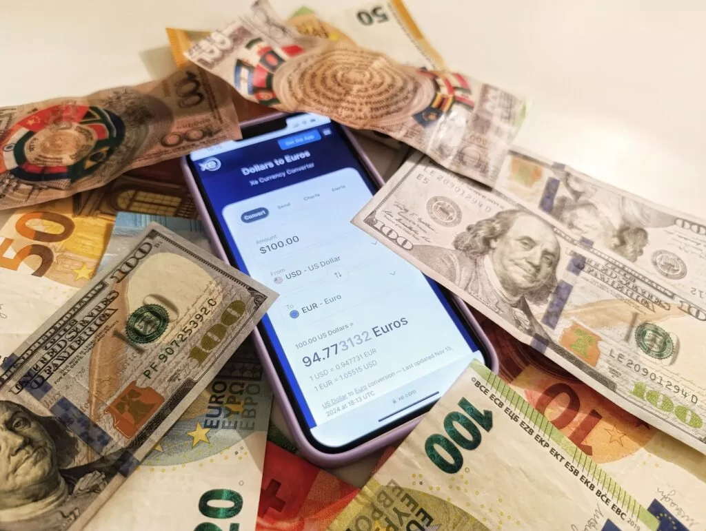 A smartphone displaying a currency converter surrounded by dollar and euro banknotes