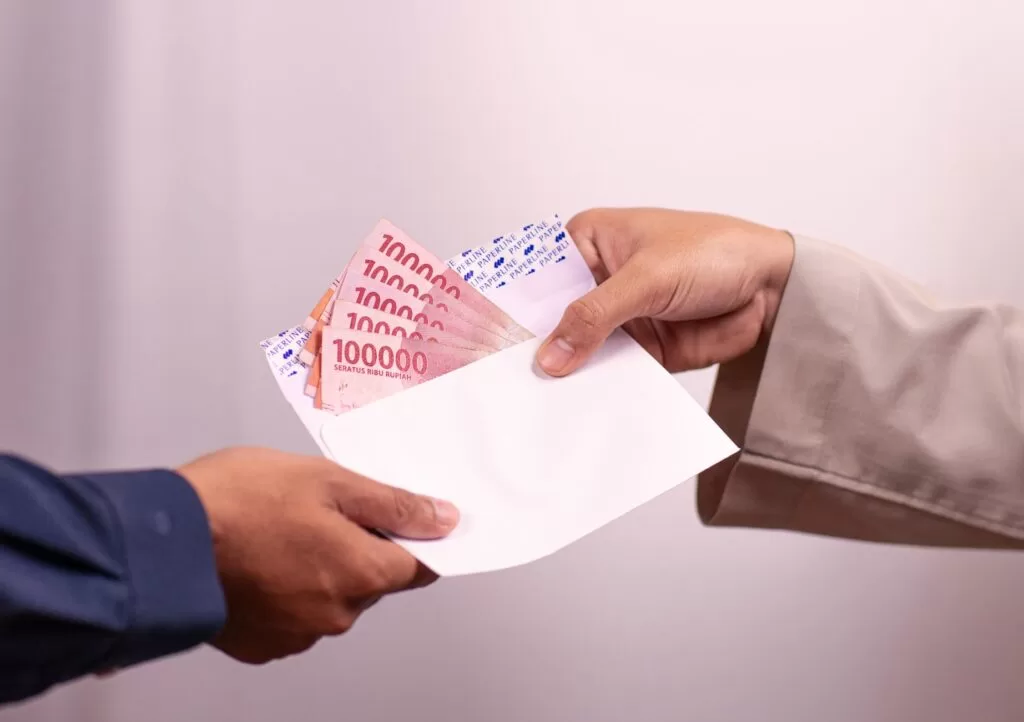 Hands giving and receiving Indonesian rupiah in an envelope during a financial transaction.