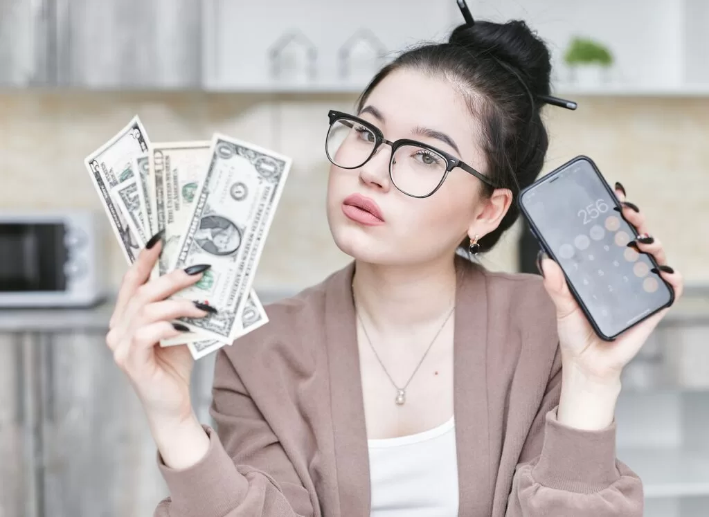 Woman holding cash and a smartphone with a calculator