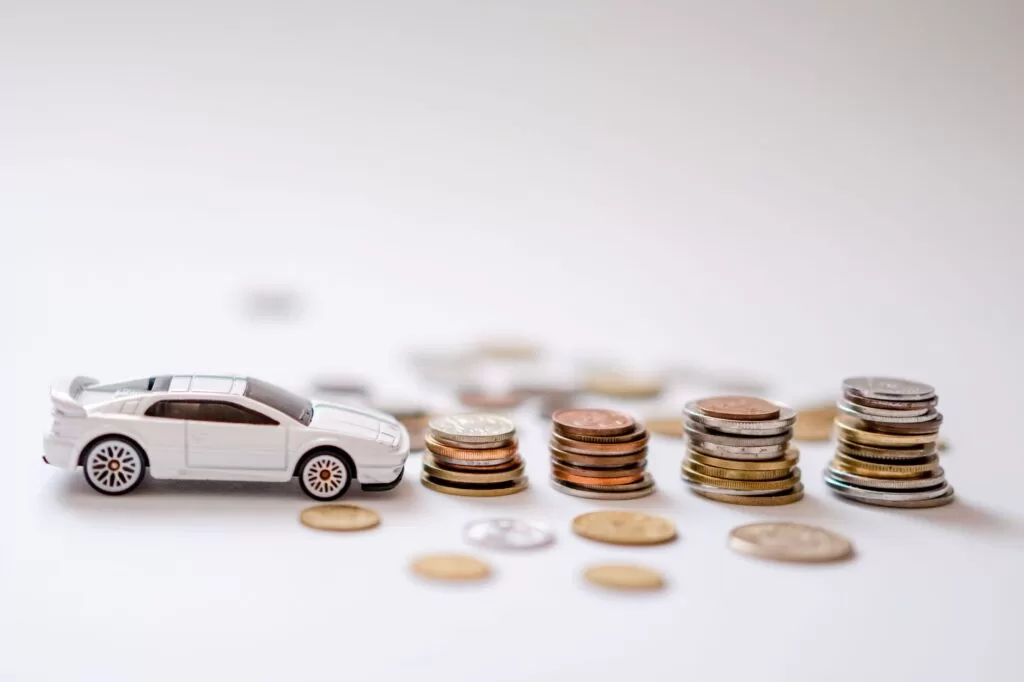 White toy sports car beside stacks of coins on a white background, representing used car price comparisons and budgeting.